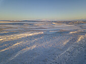 Aerial view of snow-covered expanses meeting the horizon under a tranquil sky, casting long shadows across the frozen landscape, Karasjok, Finnmark, Norway.