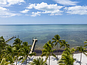 Luftaufnahme von Palmen, die den weißen Sandstrand säumen, der auf den ruhigen türkisfarbenen Ozean trifft, mit Docks, die sich ins Wasser erstrecken, Islamorada, Florida, Vereinigte Staaten.
