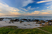 Blick auf einen felsigen Strand, der unter einem von Sonnenuntergangstönen durchzogenen Himmel auf den weiten Ozean trifft, eine ruhige Küstenszene, Hermanus, Westkap, Südafrika.