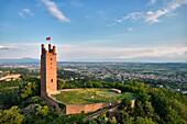 Aerial view of the striking Rocca di Federico II, a medieval brick tower topped with a flag, surrounded by green hills, San Miniato, Tuscany, Italy.