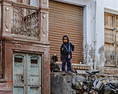 Bikaner, Indien - 24. Juni 2025: Blick auf ein Kind inmitten der rustikalen Architektur, der verwitterten Fensterläden und des leisen Motorrads, ein Tableau des ruhigen Stadtlebens.