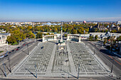 Aerial view of the vast Heroes' Square, its geometric pavement shimmering under the sun, framed by the Museum of Fine Arts and the Palace of Art, Budapest, Hungary.
