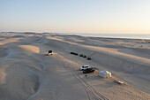 Luftaufnahme von Fahrzeugen und Zelten auf den Sanddünen in Küstennähe, eine ruhige Szene unter dem sanften Licht des Himmels, Muscat, Muscat Governorate, Oman.