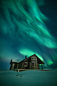 Lofoten Islands, Norway - 15 March 2023: View of a cozy cabin nestled in the snowy landscape, illuminated by the ethereal dance of the aurora borealis.