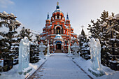 View of a vibrant, snow-dusted Russian Orthodox Church stands majestically between ice sculptures of angels, a cold but inviting scene, Irkutsk, Russia.