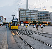 Berlin, Germany - 27 August 2019: View of a vibrant yellow tram gliding through Alexanderplatz, juxtaposed against the stark, imposing architecture of the Park Inn hotel.