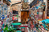 View of vibrant stacks of books create colorful walls around a cozy outdoor seating area in a hidden corner, Venice, Veneto, Italy.