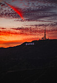View of the Hollywood sign silhouetted against a fiery sunset sky with streaks of red and orange illuminating the clouds, Los Angeles, California, United States.