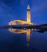 View of the Hassan II Mosque mirrored in the still water, a beacon of light against the twilight sky, illuminating the Moroccan coast, Casablanca, Casablanca-Settat, Morocco.