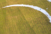 Aerial view of a lone figure trekking a snowy path cutting through a vast expanse of golden fields, a serene contrast of cold and warmth, Marktoberdorf, Bavaria, Germany.