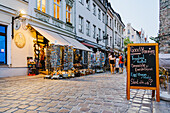 Berlin, Germany - 27 August 2019: View of a quaint street with souvenir shops and a cafe sign, bathed in warm light against the cool stone pavement.