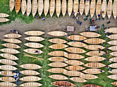 Aerial view of countless wooden boats aligned in neat rows on a grassy bank, juxtaposed with the vibrant activity of people, Bangladesh.