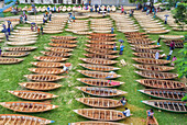 Aerial view of hundreds of wooden boats laid out on the lush green grass, creating a mesmerizing pattern of light and shadow, Bangladesh.