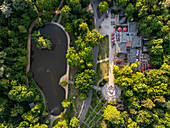 Aerial view of a serene lake surrounded by lush trees contrasts with the red umbrellas of a restaurant's outdoor seating area, Berlin, Volkspark Friedrichshain, Germany.