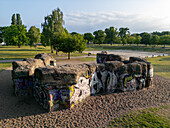 Berlin, Germany - 30 May 2025: Aerial view of a graffiti-covered, weathered structure stands starkly against the soft, golden sand in a park, framed by lush green trees under a bright sky.