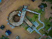 Luftaufnahme einer verwitterten, spiralförmigen Struktur, die die sandige Landschaft mit verstreutem Grün dominiert und deren Texturen im Kontrast zu den glatten Wegen stehen, Badagry, Lagos, Nigeria.