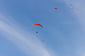 Blick auf tanzende Gleitschirmflieger unter einem grenzenlosen azurblauen Himmel, ein heiteres Spektakel von Freiheit und Abenteuer in Oderen, Grand Est, Frankreich.