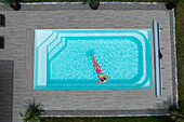 Aerial view of a woman basking on a raft in the aquamarine pool amidst the geometric patterns of the surrounding stone tiles, Strasbourg, Grand Est, France.