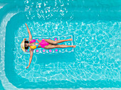 Aerial view of a woman in a bright pink swimsuit and straw hat floats serenely on a turquoise pool, a summer daydream, Strasbourg, Grand Est, France.