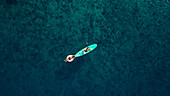 Luftaufnahme von zwei Personen, die auf einem Paddleboard und einem rosafarbenen Floß im türkisfarbenen Wasser der Adria schwimmen, Omiš, Kroatien.
