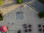 Aerial view of a checkered square contrasting sharply with the surrounding pavement, as people relax and chat in the open space, Berlin, Volkspark Friedrichshain, Germany.