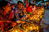 Dhaka, Bangladesh - 13 November 2018: View of people gathered in a row, their faces lit by the warm glow of numerous earthen lamps and offerings arranged on banana leaves.
