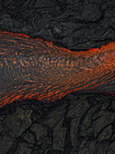 Luftaufnahme von geschmolzener Lava, die durch zerklüftetes, dunkles Vulkangestein fließt, ein feuriger Fluss, der eine karge Mondlandschaft durchschneidet, Grindavik, Region Südliche Halbinsel, Island.