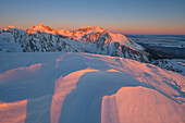 Blick auf schneebedeckte Berggipfel, die vom warmen Licht der untergehenden Sonne geküsst werden, über einem Schneefeld, Strbske Pleso, Region Prešov, Slowakei.