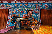 Chapai Nawabganj, Bangladesh - 14 June 2019: View of a woman focused on her sewing machine, the vibrant floral patterns around her enhancing the rich colors of her work.