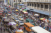 Accra, Ghana - 27 May 2017: View of a bustling street scene, a vibrant tapestry of colorful umbrellas, yellow taxis, and people near Makola Market, alive with commerce and movement.