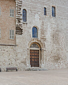 View of an ancient stone building with a dark wooden door, showcasing a blend of textures and architectural details, Gubbio, Umbria, Italy.