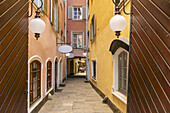 View of a narrow alleyway beckons, wooden doors framing the scene, globe lights casting soft glows upon the colorful buildings, Graz, Austria.