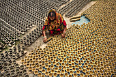 Bogura, Bangladesh - 20 May 2017: View of a woman amidst neatly arranged rows of earthen diyas, their contrasting gray and ochre hues creating an intricate tapestry of tradition and craft.