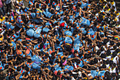 Mumbai, India - 19 August 2022: View of a human pyramid of men in blue shirts, reaching for a pot during a Dahi Handi celebration, a vibrant display of unity and tradition.