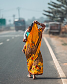 Kolkata, India - 28 January 2023: View of a woman in a vibrant yellow sari, carrying a child, walks along the road, the scene softened by a gentle haze.