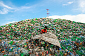 Chittagong, Bangladesh - 22 September 2022: View of a boy amidst a vast, overwhelming mountain of discarded plastic bottles under a blue sky.