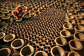 Bogura, Bangladesh - 20 May 2017: View of a woman amidst a sea of earthen pots, their warm terracotta hues creating a mesmerizing pattern across the ground.