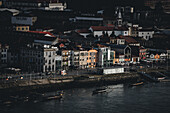 Porto, Portugal - 17. Juni 2022: Blick auf die farbenfrohen Fassaden des Stadtteils Ribeira, die kaskadenartig zum Fluss Douro hinunterfallen, wo Boote sanft im dunklen Wasser schaukeln.