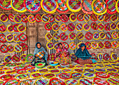 Gaibandha, Bangladesh - 04 September 2020: View of women meticulously crafting vibrant, circular handicrafts, their colorful designs a stark contrast against the rustic backdrop of the market stall.