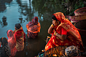 Bogura, Bangladesh - 20 November 2023: View of women in vibrant saris, their reflections shimmering in the river as they participate in a religious ceremony.