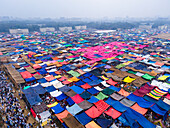 Aerial view of a sprawling tent city, a vibrant tapestry of colorful tarps, stretches out under a hazy sky, a temporary metropolis of faith and community, Dhaka, Dhaka Division, Bangladesh.