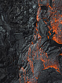 Luftaufnahme von kontrastreichen Strukturen, wo sich feurig orangefarbene Lava durch tiefschwarzes Vulkangestein schlängelt, ein Tanz von Zerstörung und Schöpfung, Grindavik, südliche Halbinselregion, Island.