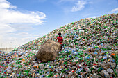 Chittagong, Bangladesh - 22 September 2022: View of a boy amidst a vast, colorful mountain of discarded plastic bottles under a bright sky.