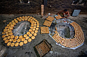 Bogura, Bangladesh - 05 February 2022: View of a worker meticulously arranging freshly baked goods around a traditional oven, creating a warm, golden tableau within the rustic brick setting.