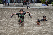 Chattogram, Bangladesch - 05. August 2023: Blick auf Kinder, die durch die überfluteten Straßen waten. Ihr Lachen hallt inmitten des Regens wider und steht in starkem Kontrast zur überfluteten Stadtlandschaft.