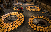 Bogura, Bangladesh - 05 February 2022: View of a worker amidst circles of palm jaggery, their golden hues contrasting sharply with the dark, earthen floor.