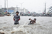 Chattogram, Bangladesch - 05. August 2023: Blick auf Kinder, die fröhlich durch die überschwemmten Straßen platschen, ihr Lachen hallt in der Stadtlandschaft wider.