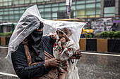 Chittagong, Bangladesch - 06. August 2023: Blick auf eine Mutter und ein Kind, die sich vor einem heftigen Regenguss unter einer behelfsmäßigen Plastikplane schützen - ein ergreifender Moment der Resilienz vor der grauen, nassen Stadtlandschaft.
