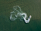 Aerial view of a boat carving swirling white patterns into the dark, tranquil waters of Lagoa de Óbidos, a dance of motion and serenity, Nadadouro, Leiria, Portugal.