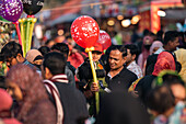 Bogura, Bangladesch - 03. November 2023: Blick auf einen Vater, der sein Kind im Arm hält, Luftballons mit leuchtenden roten Farbtupfern inmitten eines Meeres von Gesichtern und Stoffen.
